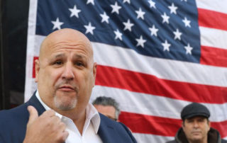 Louis Gelormino gives thumbs up in front of large American Flag